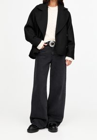 Sort oversize blazer over en cremefarvet striktrøje, kombineret med sort højtaljede vidde-ben jeans og chunky sorte støvler, fremhævet af et sølvbælte.