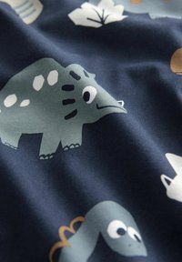 Materiał w wzory z kreskówkowymi dinozaurami w kolorach zielonym, białym i niebieskim na ciemnoniebieskim tle, gładka tekstura i zabawne elementy wzornicze.