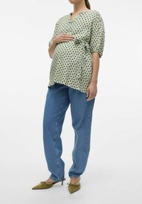 Blusa verde con stampa a cuori neri, legata in vita; jeans blu a vestibilità morbida; ballerine verde oliva a punta. Outfit semplice e casual per la maternità.