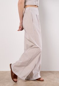 Pantalons larges à taille haute avec un motif rayé de beige clair et crème. Fabriqués en tissu léger avec une finition texturée.