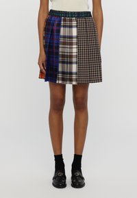 Una falda mini plisada que presenta una mezcla de varios patrones a cuadros en azul, marrón y negro. Cintura elástica, la textura de la tela es suave.