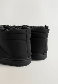 Cizme scurte negre, izolate, cu un material texturat pe partea superioară, căptușeală moale și talpă din cauciuc cu aderență; sunt dotate cu mânere pentru a fi ușor de încălțat.