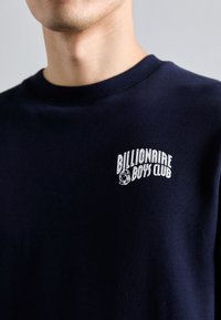 Sweat-shirt bleu marine avec un col rond et des manches courtes. Il présente un logo blanc "Billionaire Boys Club" et un graphique d'astronaute sur la poitrine.