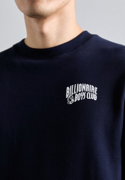 Marineblå hettegenser med rund hals og korte ermer. Har et hvitt logo "Billionaire Boys Club" og et astronautgrafikk på brystet.