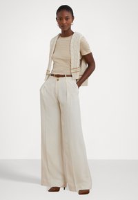Knit striped shirt in beige and cream, paired with high-waisted wide-leg cream trousers. Model wears a light cable-knit vest and brown belt.