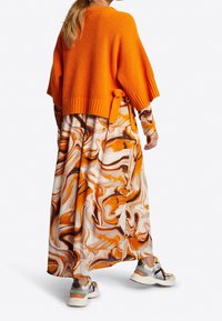 Pull court en tricot orange porté sur une longue robe marbrée aux tons orange, blanc et marron. Baskets avec des accents gris, orange et noir.