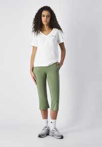 Biała bawełniana koszulka typu v-neck zestawiona z zielonymi spodniami typu crops. Sneakersy są szare, z białymi skarpetkami z logo. Prosty i casualowy design.