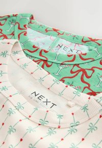 Two long-sleeve ribbed tops: one green with red cocktail and ribbon pattern, the other cream with mint bows and red hearts. Both branded.