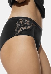 Zwarte slip van gladde stof, met een doorzichtige kanten inzet met bloemmotieven aan de zijkant. Standaard tailleband ontwerp.