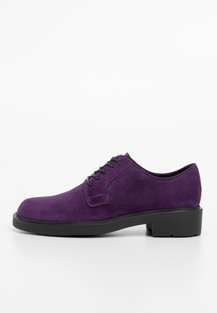 Chaussure en daim violet à lacets avec un bout arrondi, semelle en caoutchouc noir plate et détails de couture minimaliste sur les côtés. Texture lisse.