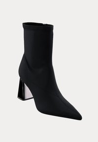 Črne gležnjače iz raztegljivega materiala s koničastim nosom, ki imajo geometrijsko peto v srebrni in črni barvi, z brezhibnimi šivi.