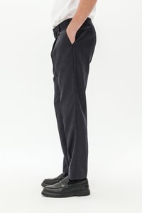 Pantaloni blu scuro realizzati in tessuto liscio, dotati di tasche laterali, con una vestibilità dritta e abbinati a scarpe slip-on nere.