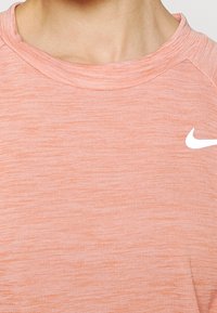 Ljus korallfärgad Nike t-shirt med en strukturerad, melerad design och rundad halsringning. Vit swoosh-logotyp placerad på vänster bröstområde.