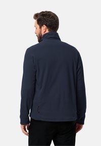 Giacca in pile navy con colletto alto, maniche lunghe e cuciture piatte. Presenta un'etichetta con marchio all'orlo. Tessuto liscio e vestibilità casual.