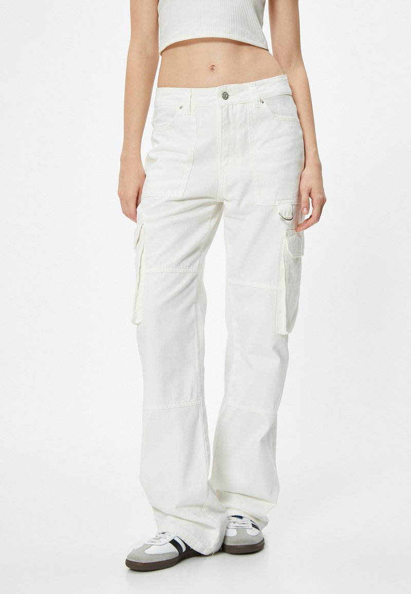 Los pantalones cargo blancos cuentan con un ajuste relajado, múltiples bolsillos laterales y una robusta tela de algodón. El diseño incluye costuras cosidas y un pequeño acento de hardware.