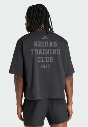 Homme avec dreadlocks portant un t-shirt noir Adidas avec l'inscription "ADIDAS TRAINING CLUB 24/7" et un short noir, vu de dos.