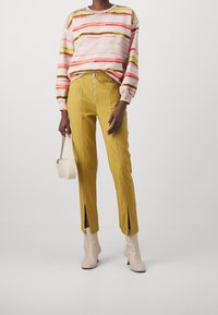 Flerfärgad sweatshirt med horisontella ränder i rosa, gult och brunt; gula byxor med framfickor med dragkedja och sidodelar; beigea ankelskor.