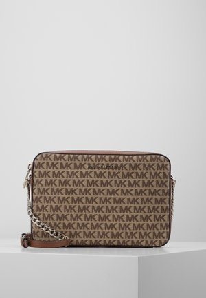 Sac bandoulière marron Michael Kors avec motif répétitif du logo MK, bandoulière chaîne dorée et fermeture éclair sur un piédestal blanc.