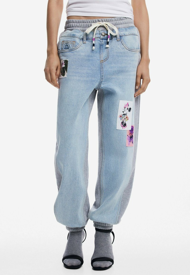 Lichtblauwe denim joggerbroeken met een grijze elastische tailleband, een trekkoord en bloemenpatches aan de voorkant. Losse pasvorm met ribbels aan de boorden.