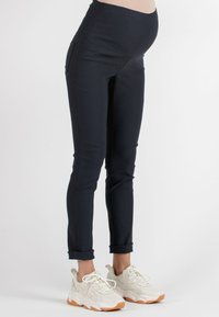 Navy maternity pants with a high waistband and side pockets, made from a stretchy material. Paired with white sneakers featuring orange accents.