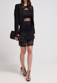 Svart spetsklänning med en figurnära silhuett, lager med spetsdetaljer, kombinerad med en kort svart jacka och en texturerad svart clutchväska.