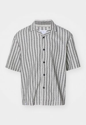 Chemise à manches courtes en tissu texturé, présentant un motif rayé noir et blanc avec cinq boutons noirs sur le devant.