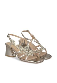 Sandalias de tacón plateadas metálicas con punta abierta, diseño de tiras adornadas y un resistente tacón cuadrado. Textura suave con acentos decorativos.