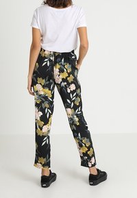 Pantalones negros con estampado floral que presentan un vibrante patrón de flores rosas y amarillas, hechos de una tela suave con un corte relajado y cinturilla elástica.