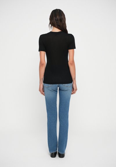 Tricou negru cu mânecă scurtă, cu un design ajustat, asortat cu blugi evazați de culoare albastru deschis. Materialul pare moale și ușor transparent.
