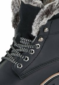 Botas de cuero negro con adornos de pelo sintético, ojales hexagonales y cordones en blanco y negro. Suela resistente con toques de marrón claro.