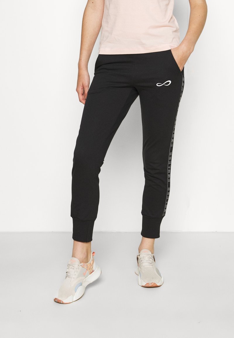 Svarta joggerbyxor med tapered passform, vit logodetalj, sidostråkar med text och elastiska muddar. Burit med ljusa sneakers.