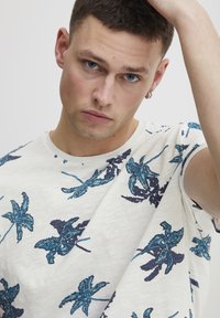 Camiseta de manga corta blanca con un patrón floral en azul y oscuro marino. Corte informal, escote redondo, textura suave y diseño minimalista.