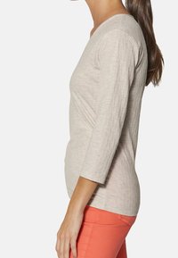 Beżowa bluzka o fakturze z rękawami do łokcia, zestawiona z koralowymi spodniami. Bluzka ma delikatny wzór pikowania na całej powierzchni.