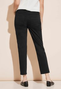 Pantalones de mezclilla negros con un diseño ajustado, estilo de cinco bolsillos y dobladillo remangado. Textura suave, detalles de costura mínimos y un corte clásico.