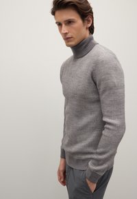 Grauer Rippturtleneck-Pullover aus weichem Stoff, mit langen Ärmeln und körpernahem Schnitt. Dazu graue Hose kombiniert.