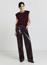 Bordeauxfarbenes ärmelloses Stricktop mit dekorativem Kragen, kombiniert mit hoch taillierten glänzenden bordeauxfarbenen Kunstlederhosen mit weitem Schnitt.