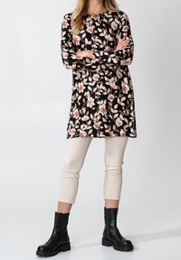 Robe noire à fleurs avec manches longues, ornée de fleurs roses et beiges, associée à des leggings courts de couleur crème et des bottines noires.