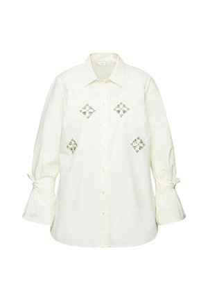 Witte button-up shirt met geborduurde diamantpatronen in zilver, voorzien van belmouwen die bij de manchetten zijn gestrikt. Gemaakt van lichte, zachte stof.