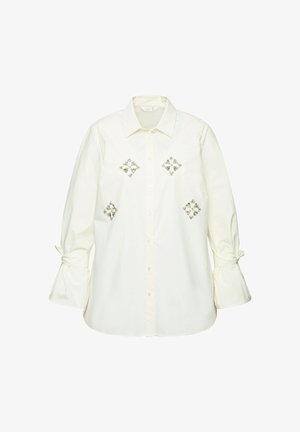 Witte button-up shirt met geborduurde diamantpatronen in zilver, voorzien van belmouwen die bij de manchetten zijn gestrikt. Gemaakt van lichte, zachte stof.