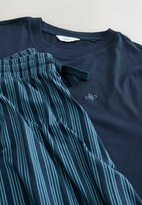 Tumši zils kokvilnas T-krekls ar apaļu kaklu, pārī ar tumši zilām un ziloņzaļām svītrainām pidžamu biksēm, kurām ir elastīga josta un aukla.