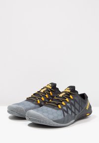 Scarpe da atletica grigie con una texture a nido d'ape, dettagli neri, lacci gialli e una suola robusta. Presentano un design a profilo basso per una maggiore flessibilità.