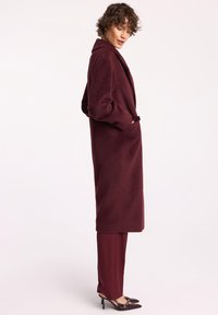 Burgundowa długa kurtka o fakturowanym wykończeniu, z szerokimi rękawami i przednimi kieszeniami, w połączeniu z dopasowanymi spodniami i czółenkami z wąskim noskiem.