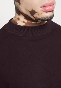 Bordowy sweter z dzianiny z żeberkowym okrągłym dekoltem, dopasowany krój, charakteryzujący się gładką fakturą i minimalnymi detalami.