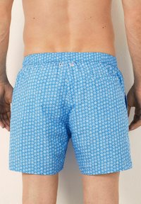 Costume da bagno blu con un motivo di stelle bianche. Realizzato in tessuto leggero con vita elastica e due tasche laterali.