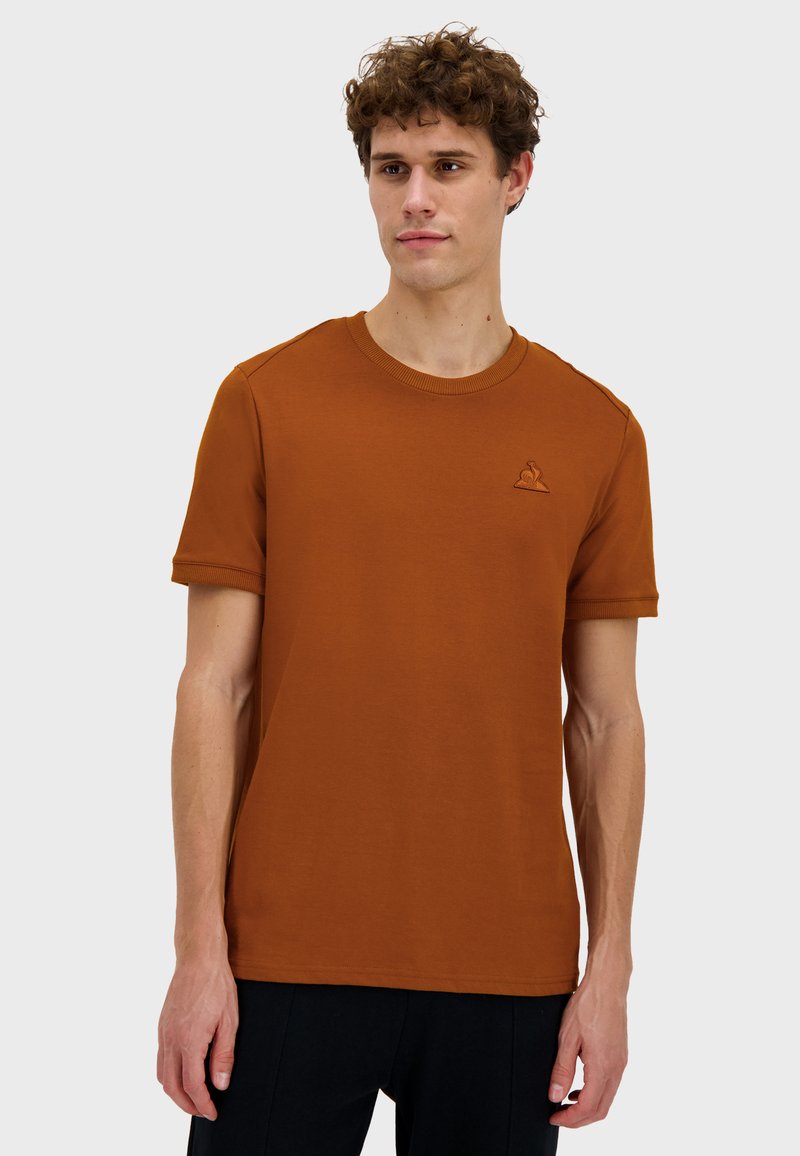 T-shirt a maniche corte e collo rotondo in cotone marrone terra. Presenta un piccolo logo ricamato sul petto e polsini a coste.