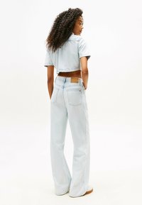 Giacca cropped in denim chiaro e jeans a gamba larga, caratterizzati da una texture liscia, dettagli cuciti e un'etichetta sul retro dei jeans.