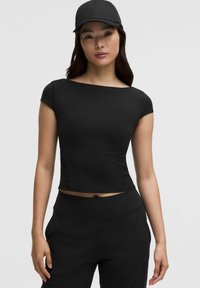 Top court noir à manches courtes et décolleté large, en matière extensible. Associé à un pantalon noir taille haute assorti et une casquette.