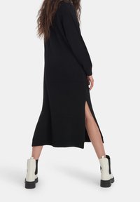 Lång svart stickad klänning med sidoklyftor, parat med vita och svarta ankelskor med en grov sula. Enkel, sammanhängande design.