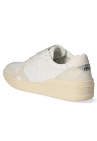 Sneaker in pelle bianca con un accento in camoscio, design con lacci, suola in gomma beige e un logo sul lato. Include un'etichetta con "est. 1995."