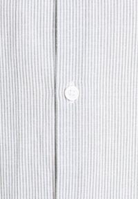 Tissu de chemise blanche avec de fines rayures verticales grises et un seul bouton blanc au centre, montrant le détail de l'avant de la chemise.